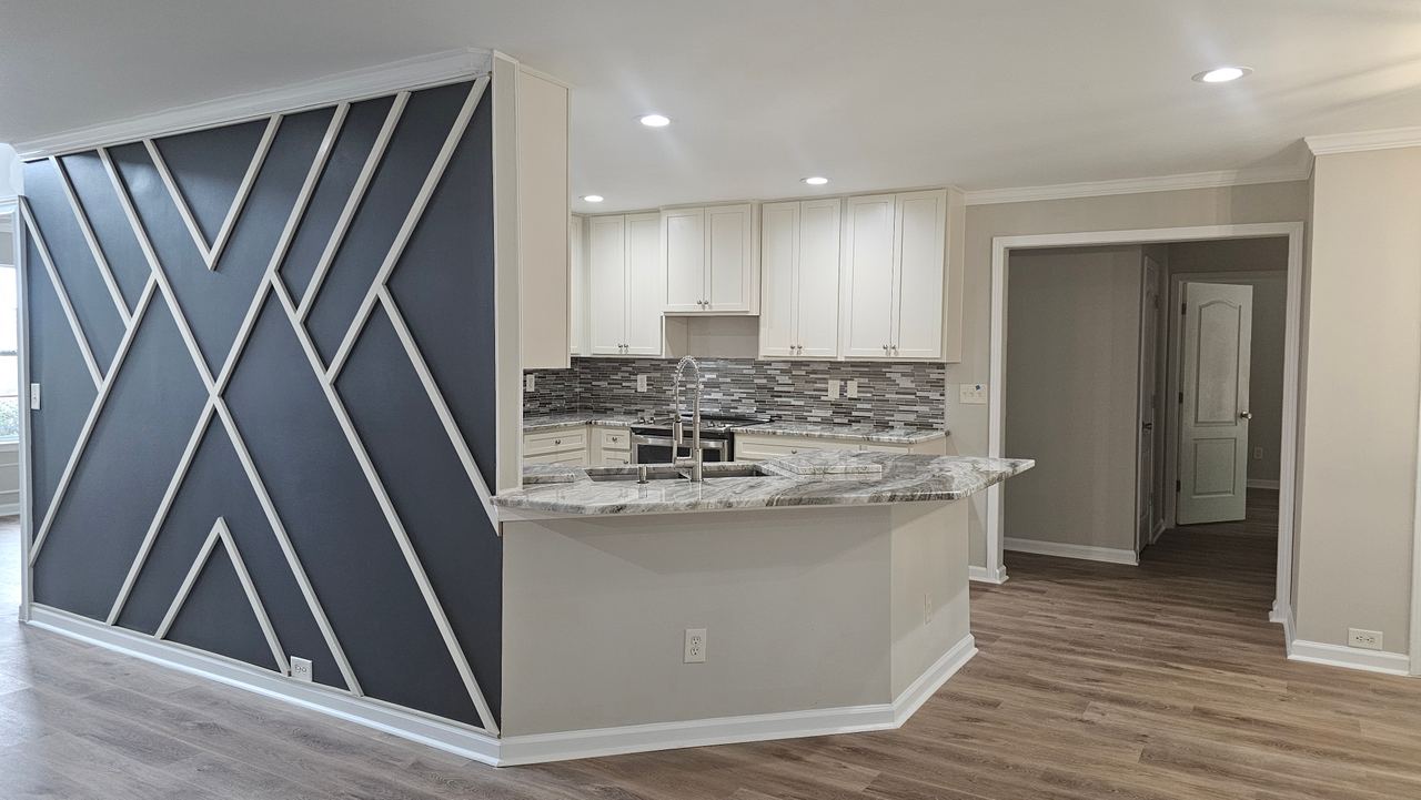 The finished kitchen: white shaker cabinets, a mosaic tile backsplash and a granite peninsula, with the geometric accent wall alongside.