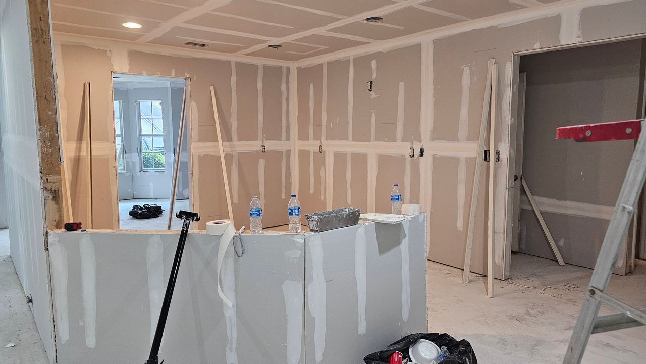The kitchen stripped back to new drywall, taped and mudded, with the island framed and the floor still bare.