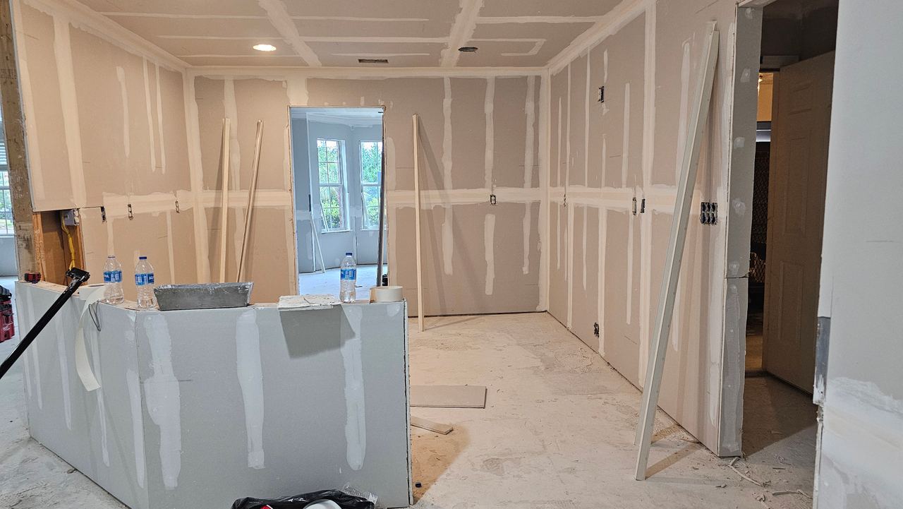 The same room at drywall stage from the opposite corner, its doorways framed and openings cut.